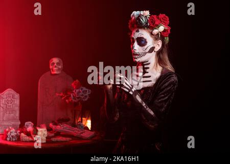 Dama della morte che scatta foto su smartphone e cattura immagini horror con la fotocamera del telefono cellulare. Donna con cranio make up e costume messicano Halloween in piedi in studio, santo dios de los muertos. Foto Stock