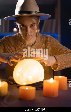 Soothsayer usando la sfera di cristallo per predire il futuro al tavolo nell'oscurità con le candele. Raccontare fortuna Foto Stock