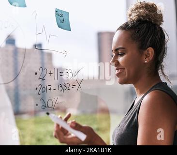 Mantenere il successo nelle sue previsioni. Una giovane donna d'affari che scrive su una parete di vetro in un ufficio. Foto Stock