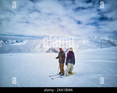 Sciatore e snowboarder in piedi in cima alla montagna contro il cielo blu e il panorama delle montagne. Due amici attivi hanno vacanza sul concetto di stazione sciistica. Antenna Foto Stock