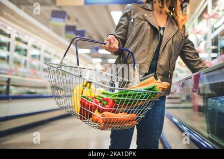 Con questa qualità non c'è da stupirsi se fa shopping qui: Una donna che tiene un cestino mentre fa shopping in un negozio di alimentari. Foto Stock