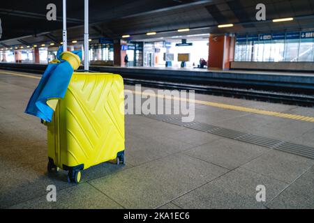 giallo valise con bandiera ucraina alla stazione ferroviaria Foto Stock