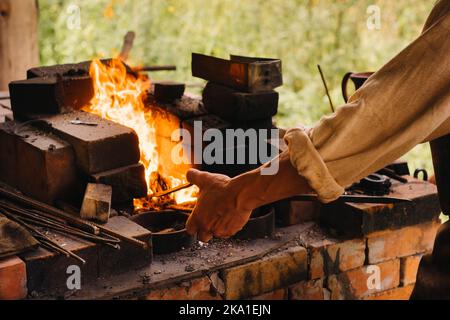 Un fabbro indurisce l'acciaio ad alta temperatura in una fornace fatta in casa nel villaggio Foto Stock