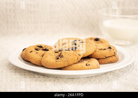 Biscotti con gocce di cioccolato in primo piano e bicchiere di latte. Foto Stock
