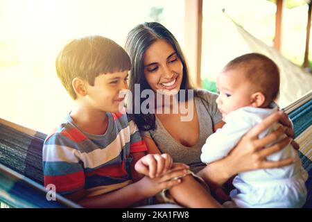Le due persone più importanti della mia vita: Una madre allegra che si rilassa su un'amaca con i suoi due ragazzini fuori casa durante il giorno. Foto Stock