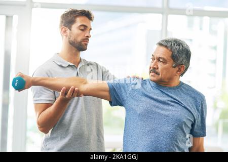 Un giovane fisioterapista maschile che assiste un paziente anziano nel recupero. Foto Stock