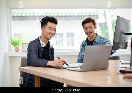 Due giovani programmatori maschi asiatici professionisti o fotoreattori che lavorano insieme in ufficio, discutendo e brainstorming. Foto Stock