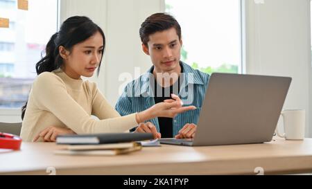 Due giovani lavoratori asiatici professionisti che si sono concentrati sulla collaborazione, guardando lo schermo del notebook e condividendo idee creative tra loro. Foto Stock