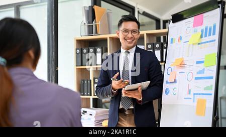 Esperto e professionale imprenditore asiatico o consulente finanziario maschile che presenta il suo progetto finanziario ai suoi colleghi nel roo della riunione Foto Stock