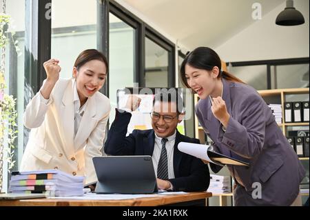 Gli imprenditori asiatici sono entusiasta di controllare i risultati del progetto su tablet, celebrare insieme il loro successo, gioire della vittoria, mostrare trionfi Foto Stock