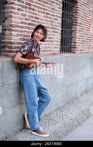 Ragazzo taiwanese sorridendo e suonando la chitarra acustica Ukulele. Foto Stock