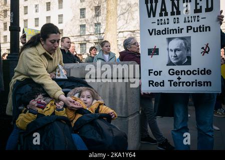 Londra, Regno Unito. Marzo 19, 2022. Una donna nutre i suoi figli a una manifestazione contro l'invasione russa dell'Ucraina, accanto a un banner che denuncia Putin. Foto Stock