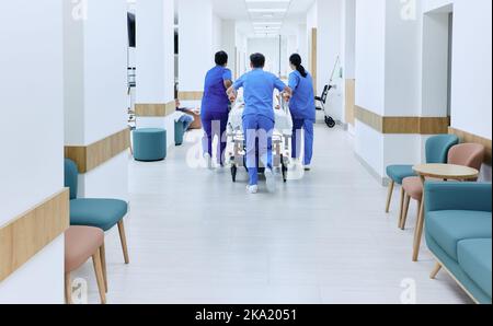 squadra di assistenza ospedaliera precipitosamente facendo girare il paziente sulla barella medica al pronto soccorso dell'ospedale, vista posteriore. Lavoro di squadra medica di emergenza Foto Stock