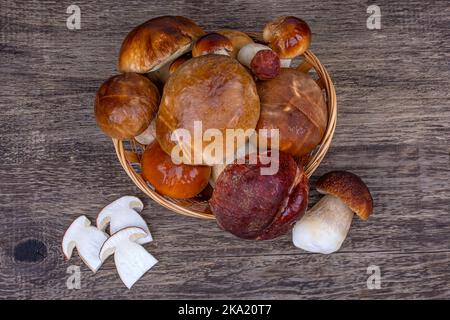 Cesto di vimini con porcini interi e tagliati su fondo ligneo, primo piano Foto Stock