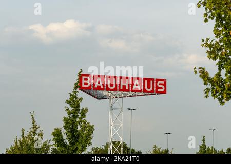 Le lettere Bauhaus del negozio di ferramenta tedesco in alto nel cielo. Pubblicità su un parcheggio. Gli alberi verdi sono davanti al cielo nuvoloso. Foto Stock