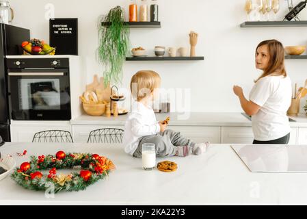 Preparandosi per Natale. La mamma sta lavorando in cucina mentre suo figlio si siede e la guarda Foto Stock