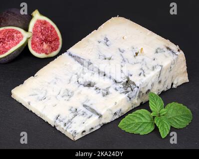 deliziosa gorgonzola italiana con foglie di menta e fichi su un piano di ardesia nera, gustoso pezzo di formaggio blu originale Foto Stock