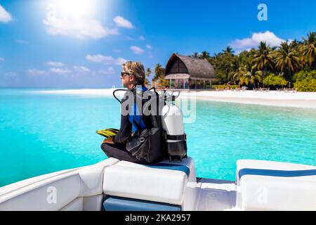 Un subacqueo con il suo equipaggiamento da immersione siede di fronte a una barca Foto Stock
