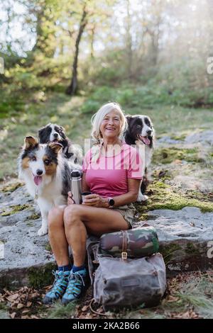 Donna anziana che si rompe durante la camminata dei suoi tre cani nella foresta. Foto Stock