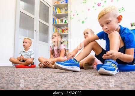 Esperienza di terapia occupazionale infantile. Bambini di età elementare in terapia di gruppo. Allievi in classe seduti sul pavimento. Foto Stock