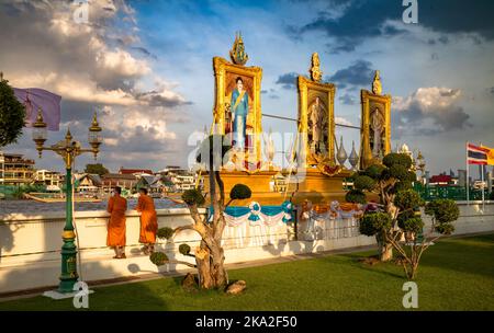 Due monaci buddisti si trovano a guardare il fiume Chao Phraya accanto agli enormi ritratti dorati del re tailandese, sua moglie e sua madre al Wat Arun di Bangkok Foto Stock