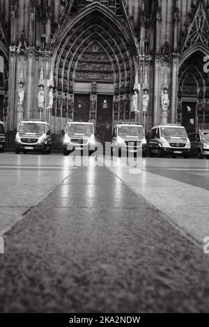 Un colpo in scala di grigi di fila di Mercedes-Benz Sprinter auto di polizia di fronte alla Cattedrale di Colonia in Germania Foto Stock