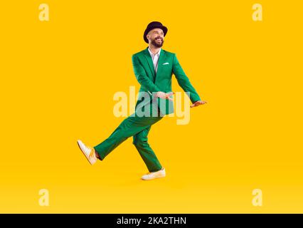 L'uomo allegro in vestito verde moderno e cappello sta ballando e divertendosi celebrando il giorno di San Patrizio. Foto Stock