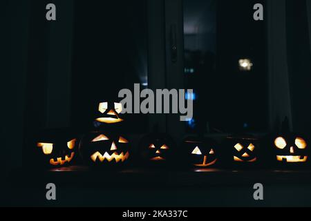 Profondità di campo bassa (fuoco selettivo) dettagli con varie zucche di Halloween intagliate (Jack-o-lanterne) al buio con candele elettriche all'interno. Foto Stock