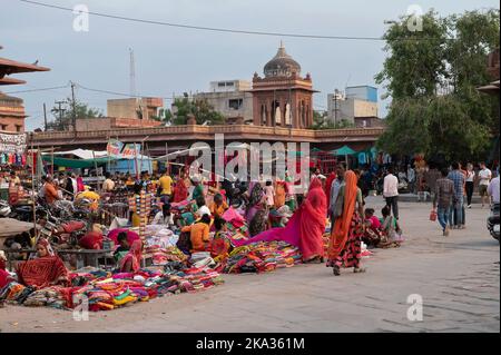 Jodhpur, Rajasthan, India - 20.10.2019 : Rajasthani Womens vestiti che sono venduti al mercato sardo famoso e Ghanta ghar Torre di orologio in serata. Foto Stock