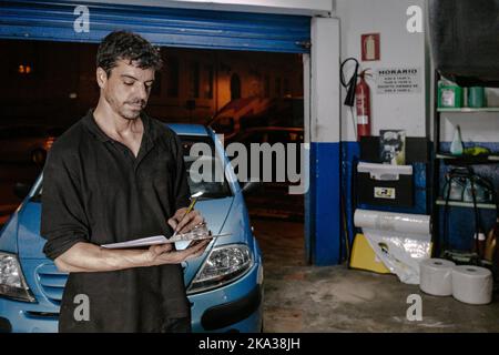 Il tecnico scrive sulla clipboard vicino all'auto in garage Foto Stock
