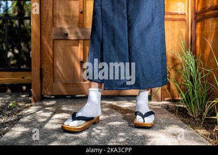 Vista al piano terra dei piedi dell'uomo in costume kimono, calze di scarpe di geta tabi nel giardino all'aperto in Giappone da porta d'ingresso moderna in legno Foto Stock