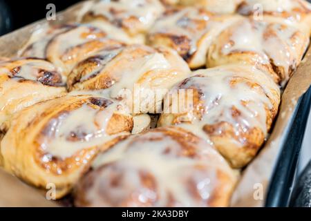 Macro closeup di grandi panini alla cannella cotti crudi e cotti rotolano su foglio di carta pergamena con zucchero dolce glassa dessert su vassoio Foto Stock