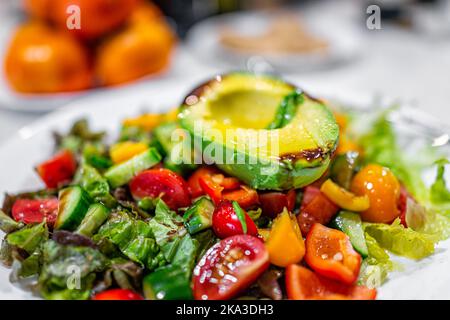 Macro primo piano di verdure tagliate a fette su piatto bianco con insalata vegana fresca con insalata di lattuga romana, pomodori, peperoni e metà avocado Foto Stock