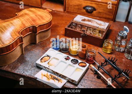 Dall'alto tavolo in legno con vernici e olio vicino al mix palette e violino in bottega di luziatore Foto Stock