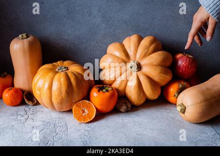 Ancora la vita di mano che indica le verdure autunnali assortite, le zucche, le mele, i persimmoni, i tangerini e le nocciole su fondo scuro Foto Stock