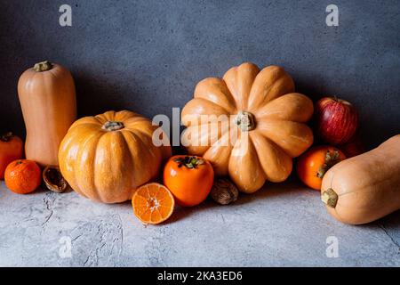 Vita morta di verdure d'autunno assortite, zucche, mele, persimmoni, tangerini e nocciole su sfondo scuro Foto Stock