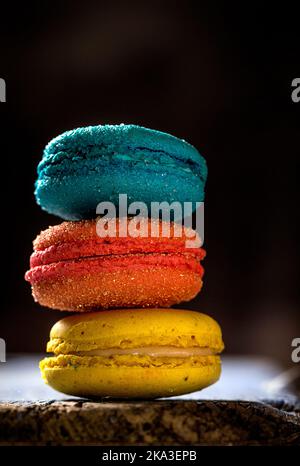 Primo piano di coloratissimi macaroni francesi con vari ripieni posti su un tavolo di legno su sfondo scuro Foto Stock