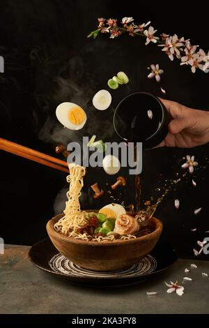 Cuocete le tagliatelle con i bastoncini e aggiungete il brodo miso al ramen, mentre le uova e la cipolla con i funghi cadono in una ciotola Foto Stock