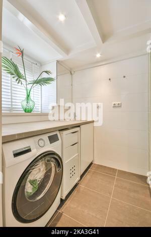 Moderna lavatrice elettrica bianca posta vicino al mobile con lavabo in una lavanderia leggera Foto Stock