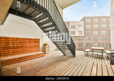 Grande terrazza con scala e panca in legno e tavolo su piastrelle contro recinzioni in mattoni e metallo Foto Stock