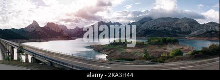 Vista panoramica del lungo ponte sul lago contro le montagne e gli alberi verdi sulla costa sotto il cielo nuvoloso Foto Stock