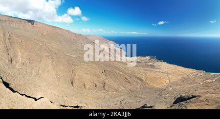 Panorama aereo panoramico del paesaggio vulcanico di montagna e di una bella costa di fronte al mare, cielo blu sfondo, isola di El Hierro, Spagna. Foto Stock