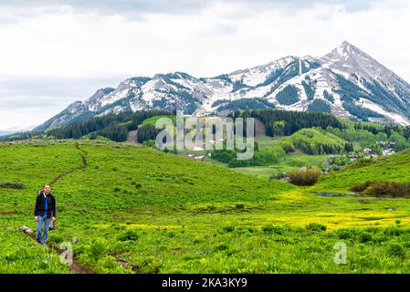 Felice giovane uomo in piedi sul sentiero Snodgrass escursione con fotocamera e vista del Monte Crested Butte, Colorado picco e giallo buttercup fiori selvatici Foto Stock