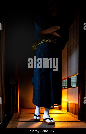 Uomo in kimono giapponese a piedi con calze geta e scarpe tabi da shoji scorrevoli porte di carta e tatami stuoia vista verticale in casa tradizionale r Foto Stock