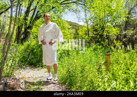 Giovane uomo felice in yukata abito bianco spa costume o abito in piedi nel giardino all'aperto in Giappone con vista sulla natura Foto Stock