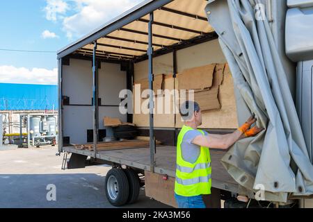 Un uomo apre una tenda su un camion per caricare le merci. Foto Stock