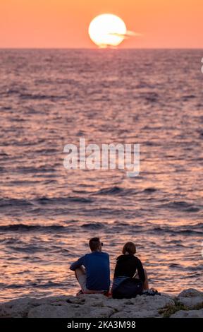 Una giovane coppia guarda il tramonto sulla costa di Paphos, Cipro. Foto Stock