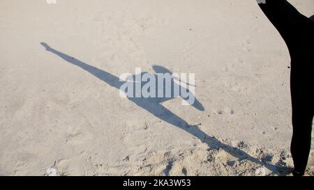 Sulla sabbia si può vedere l'ombra, la silhouette di una ragazza atletica, che esegue il sollevamento delle gambe, compie i calci, treni per combattere, la lotta con l'ombra. Movimento lento. Foto di alta qualità Foto Stock