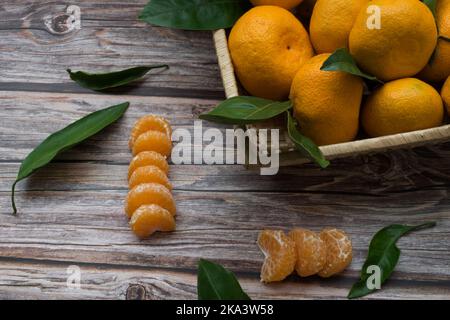 Vista dall'alto di una scatola di tangerini e segmenti di tangerini su un tavolo di legno Foto Stock