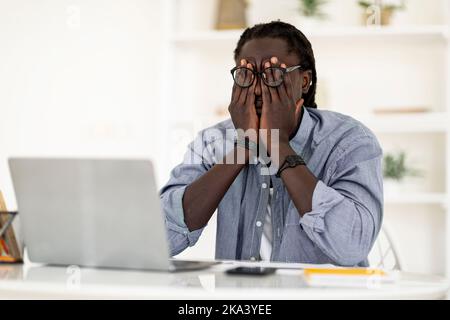 Uomo freelance nero che soffre gli occhi sforzo mentre lavora con il notebook a casa Foto Stock